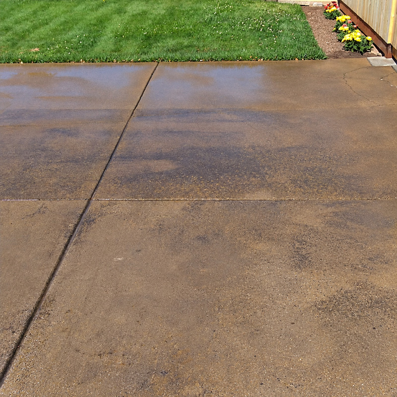 Before: stained, blotchy concrete driveway beside a lawn